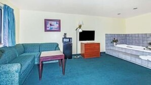 A living room with a sofa, a small table, a TV, a dresser, and a bathtub.