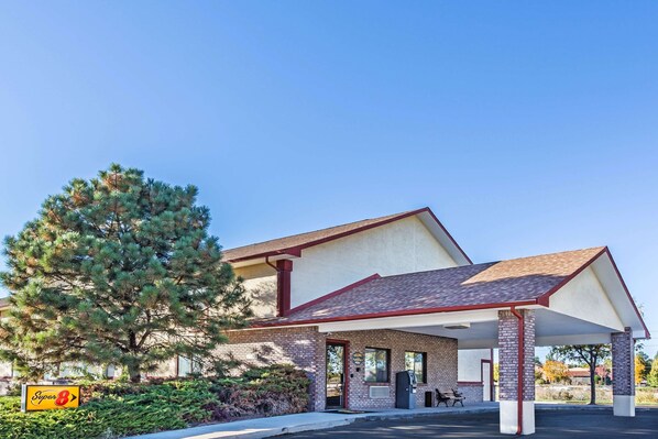 Classic hotel with a brick facade and pitched roof, offering a covered parking area and a tree-lined entrance.