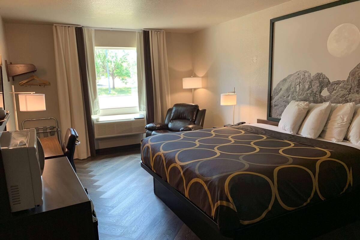 A hotel room with a bed, desk, chair, and a window with curtains.