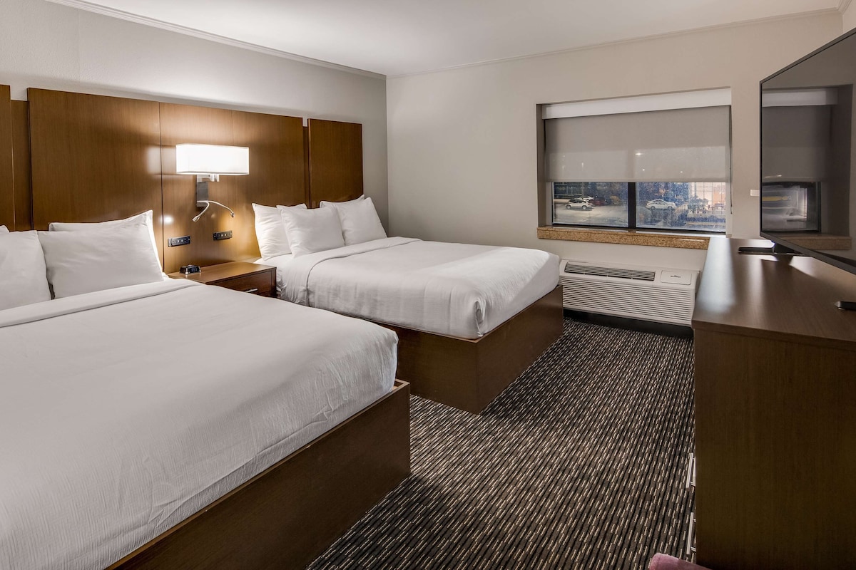 A hotel room with two beds, a desk, a chair, a TV, and a window with a city view.