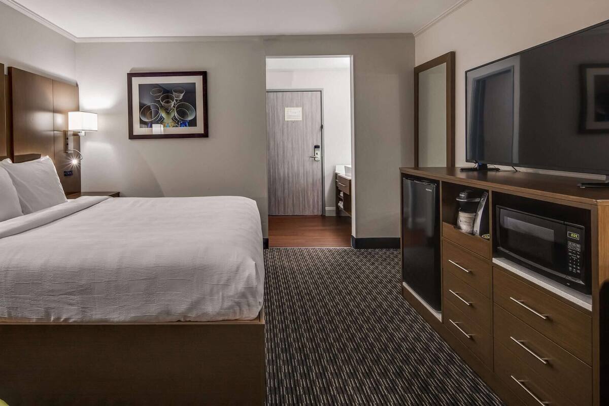 Ein Hotelzimmer mit einem großen Bett, einem Fernseher, einer Mikrowelle und einem durch eine offene Tür einsehbaren Badezimmer.