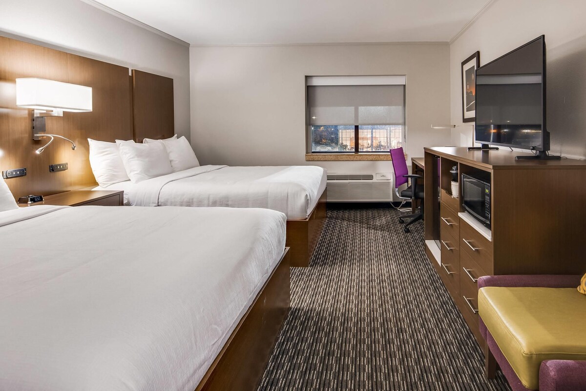 A hotel room with two beds, a TV, a desk, a microwave, and a window with a view.