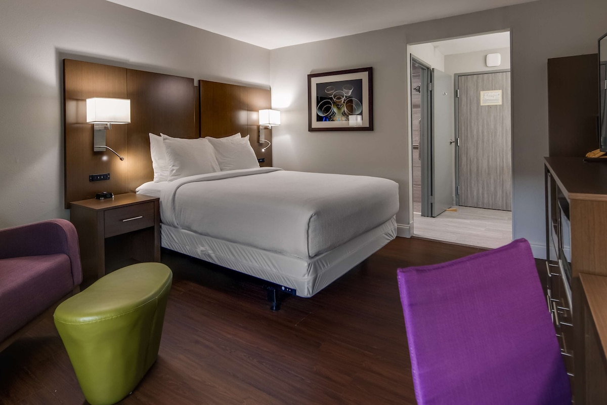 A hotel room with a bed, a desk, a chair, and a television.
