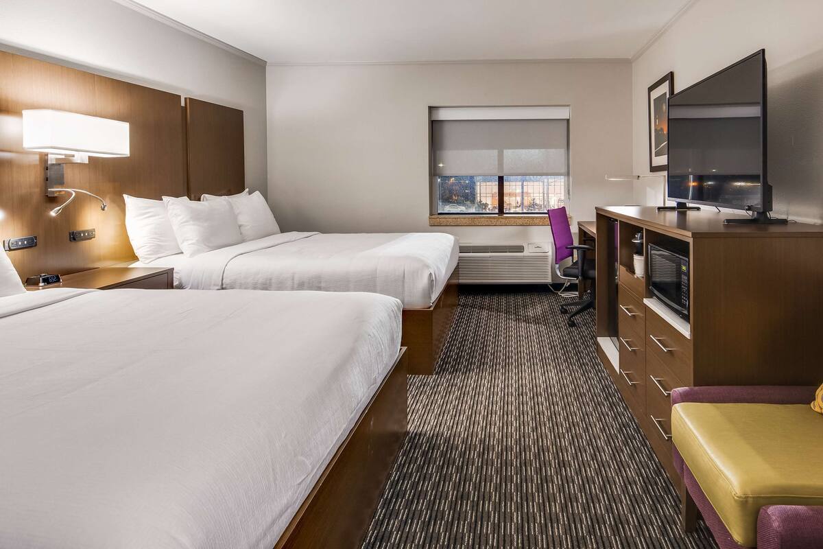 Ein Hotelzimmer mit zwei Betten, einem Fernseher, einer Mikrowelle und einem Schreibtisch mit Stuhl.