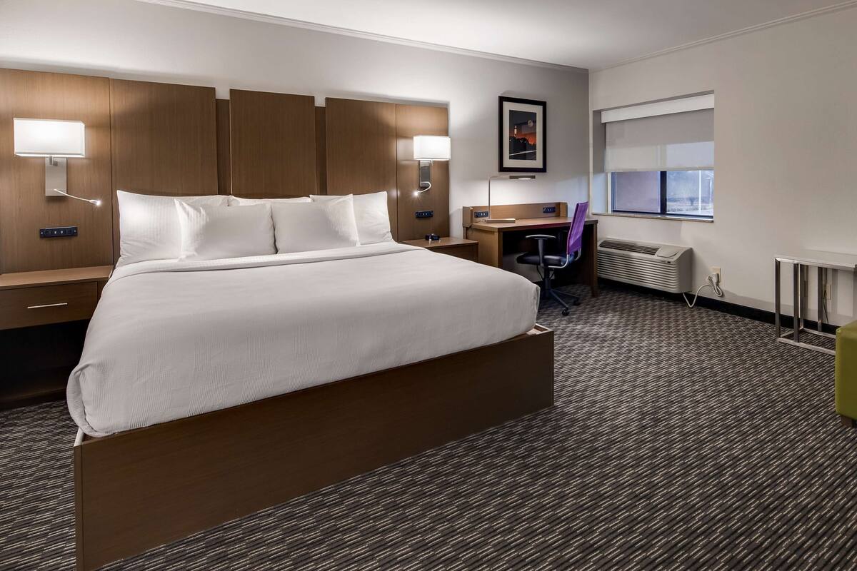 Ein Hotelzimmer mit einem großen Bett, einem Schreibtisch, einem Stuhl, einem Heizkörper und einem Fenster.
