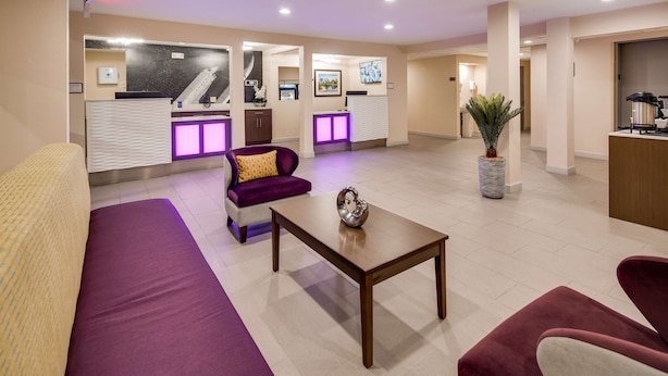 Un vestíbulo de hotel con mostrador de recepción, sofás morados, una máquina de café y una planta.
