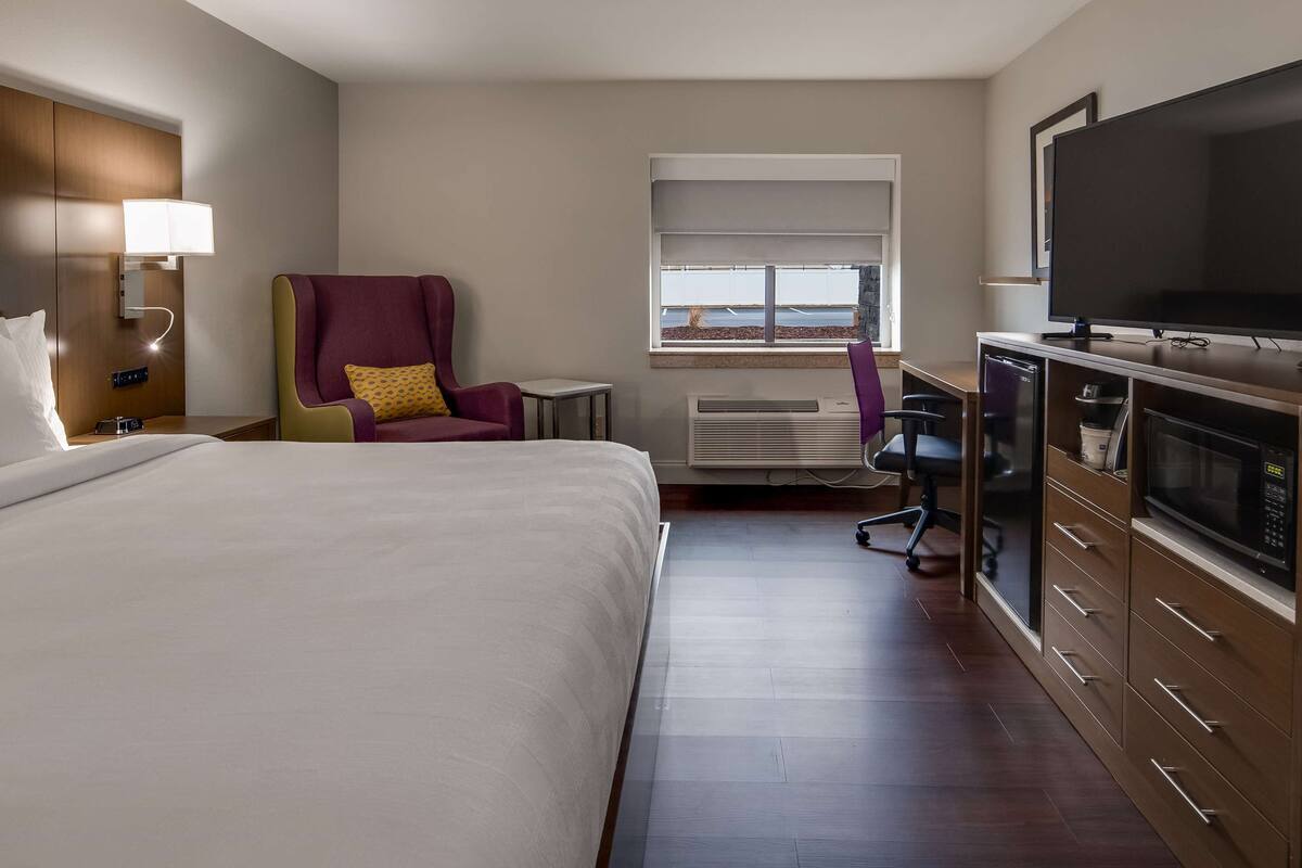 Ein Hotelzimmer mit Bett, Schreibtisch mit Fernseher, Stuhl und Fenster mit Blick.