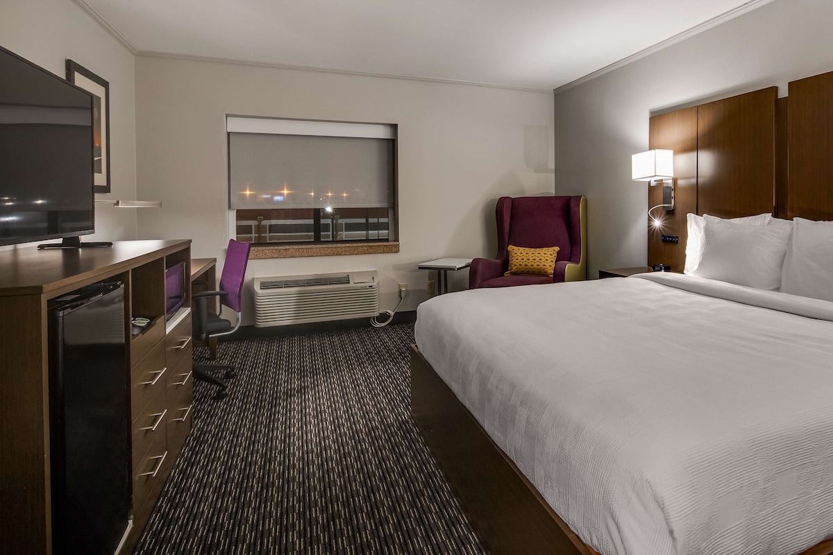 A hotel room with a large bed, a desk with a television, a chair, and a window with a view.