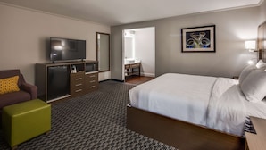 Habitación de hotel con cama, televisión, escritorio, silla, cómoda y baño visible a través de una puerta abierta.