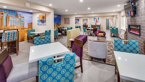 Un hall de hotel con varias zonas de estar, incluyendo mesas y sillas con tapicería estampada, una chimenea y obras de arte en las paredes.
