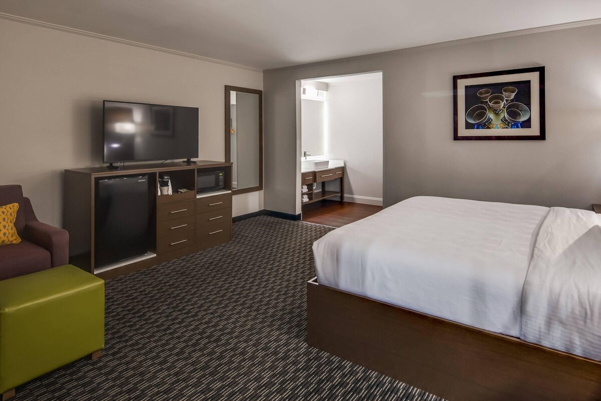A hotel room with a bed, a desk, a TV, a dresser, and a bathroom visible through an open door.