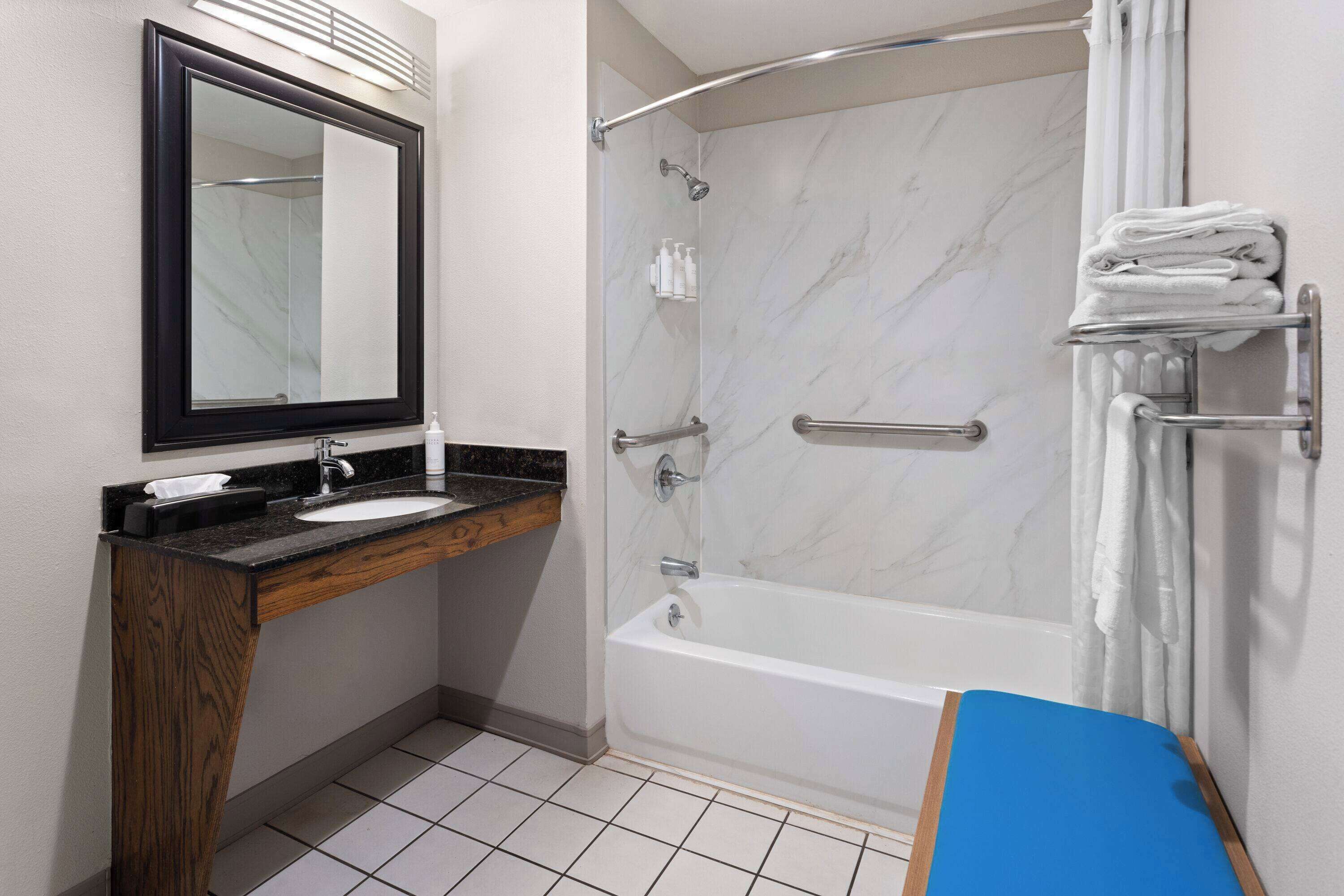 A bathroom with a marble shower, a sink with a wooden vanity, and a blue bath mat.