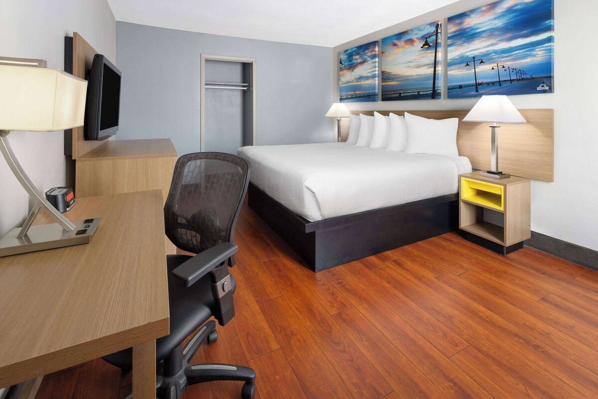 Quarto de hotel com cama, escrivaninha, cadeira, televisão e obras de arte na parede.