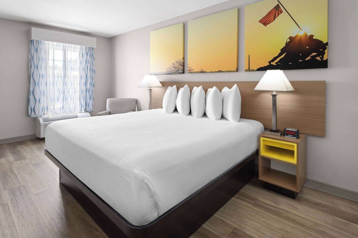 Quarto de hotel com uma cama grande, duas luminárias de cabeceira, mesa de cabeceira com relógio e janela com cortinas.