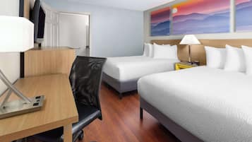 A hotel room with two beds, a desk, a chair, a TV, and a painting of a sunset.