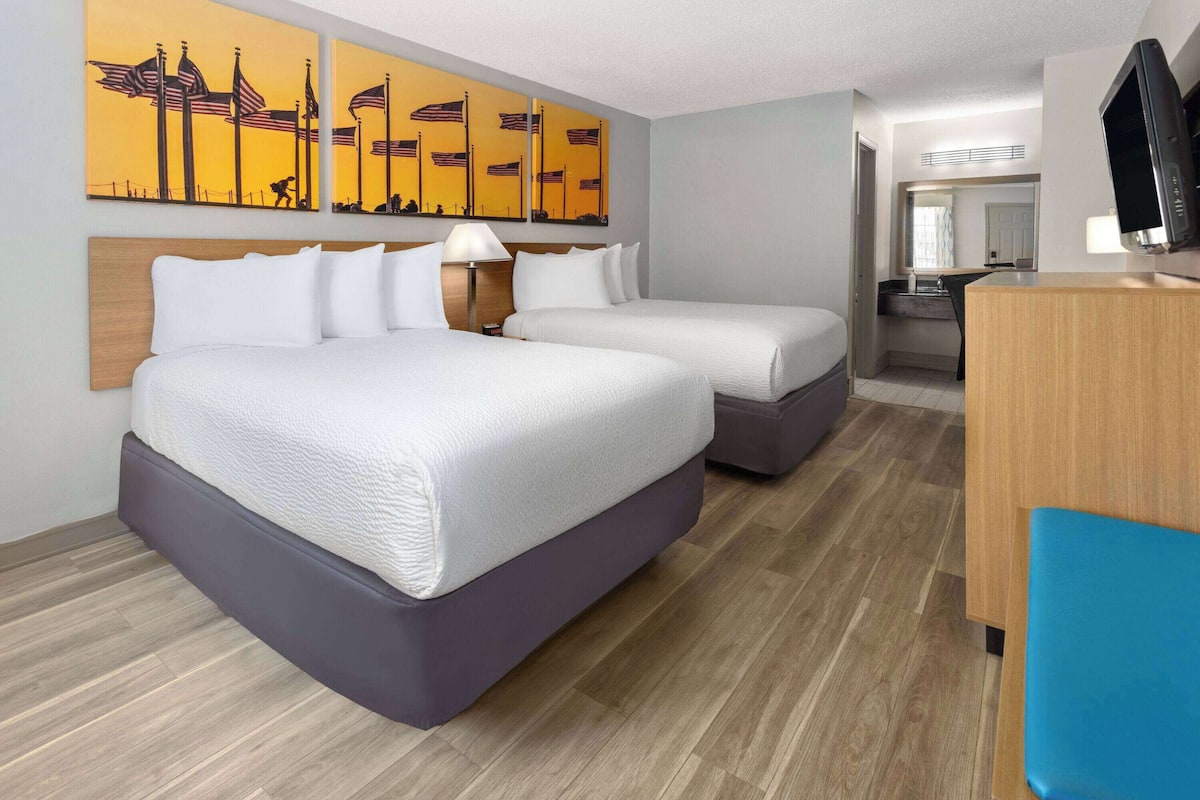 Quarto de hotel com duas camas, uma escrivaninha, televisão e obras de arte na parede.