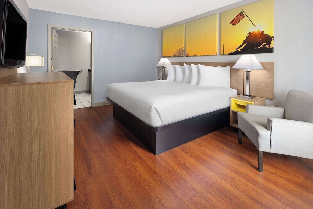 Quarto de hotel com uma cama, mesas de cabeceira, uma escrivaninha, uma cadeira e obras de arte na parede.