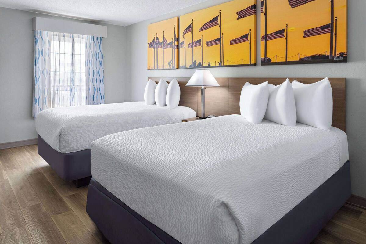 Quarto de hotel com duas camas, uma janela com cortinas e uma parede com três quadros.