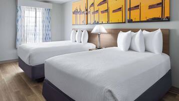 Una habitación de hotel con dos camas, un ventanal con cortinas y una pared con tres cuadros.