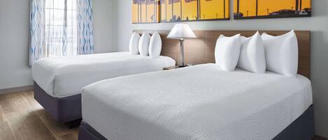 A hotel room with two beds, a window with curtains, and a wall with three paintings.