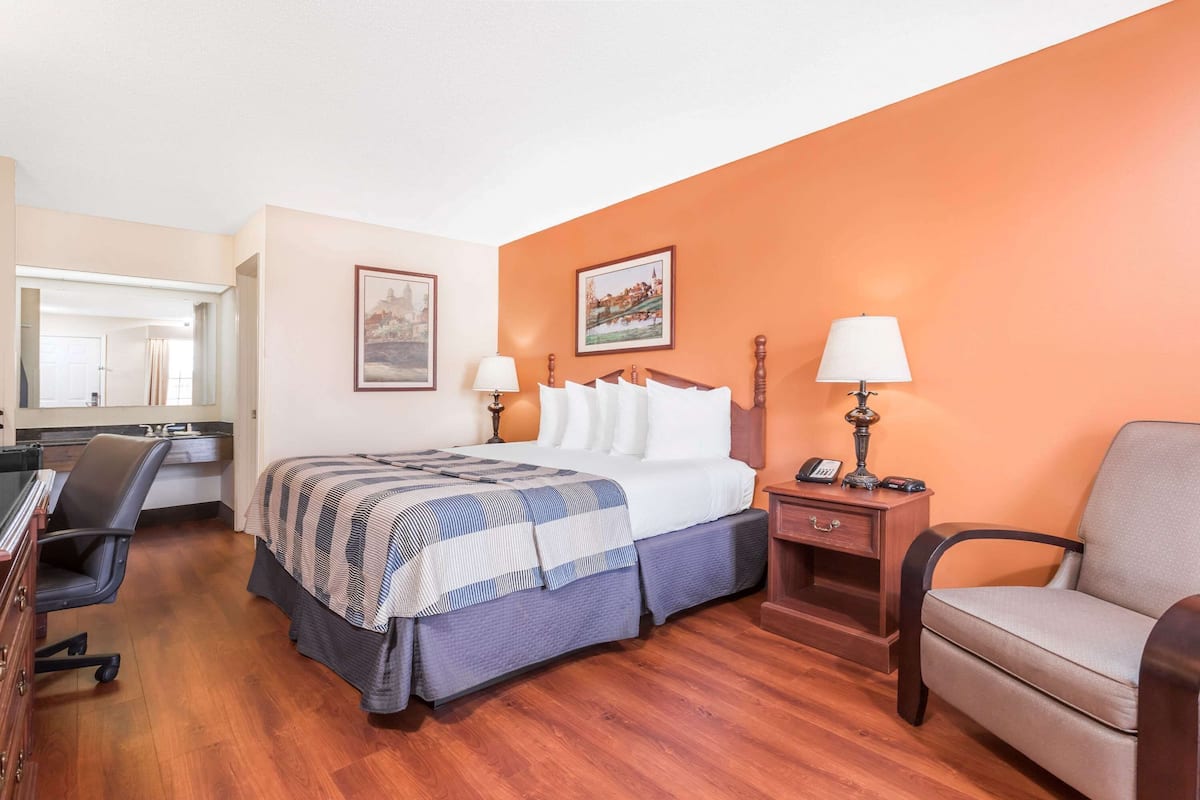 Quarto de hotel com cama, escrivaninha, cadeira e mesa de cabeceira com abajur.