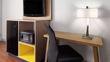 Una habitación de hotel pequeña con un escritorio de madera, una silla de oficina negra, un televisor de pantalla plana, un microondas y una lámpara.