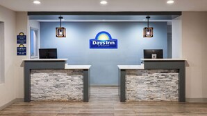 Zona de recepción con el logotipo de Days Inn, dos mostradores de recepción, detalles de pared de piedra y un cartel con la hora de registro.