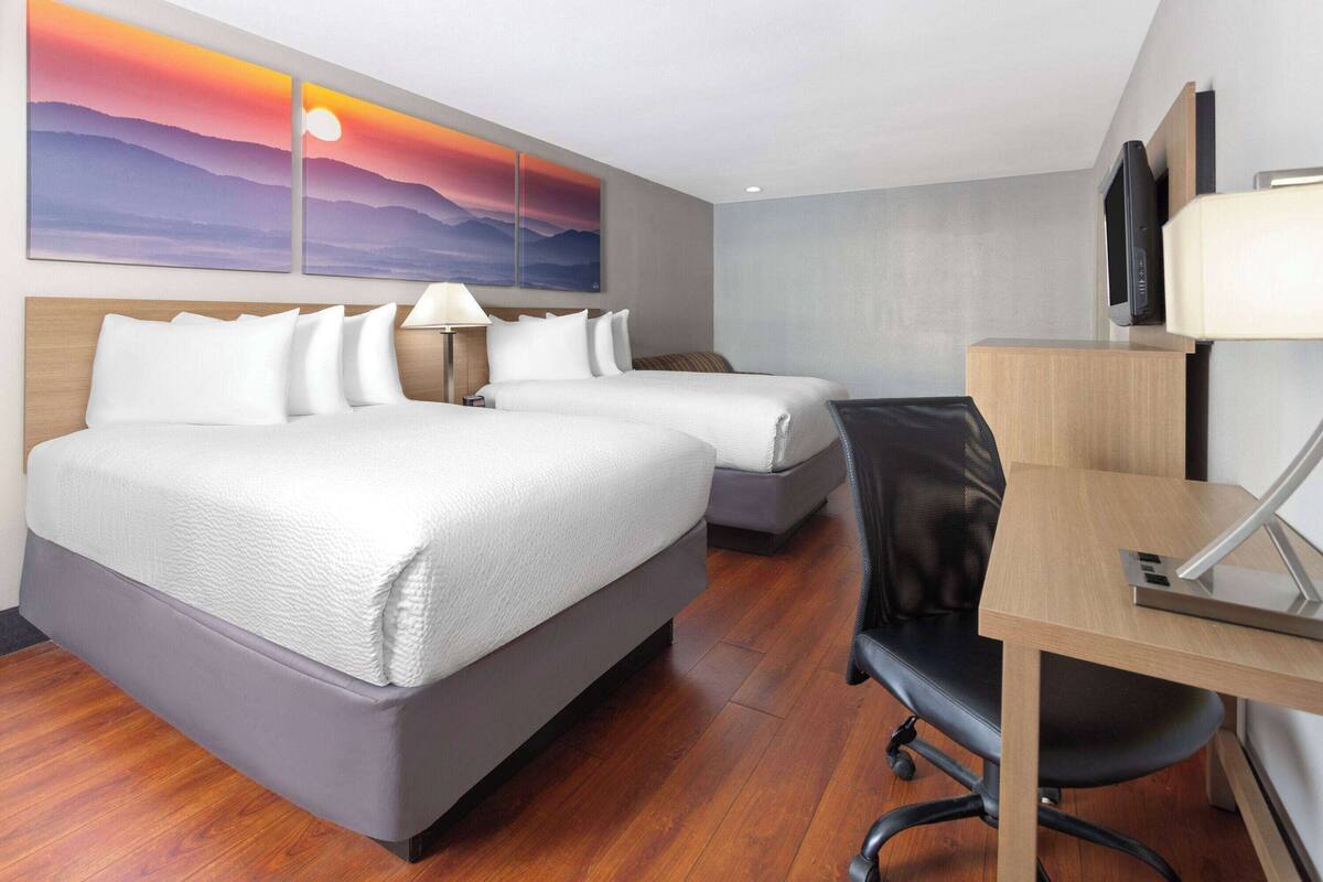 Quarto de hotel com cama, escrivaninha, cadeira e televisão.