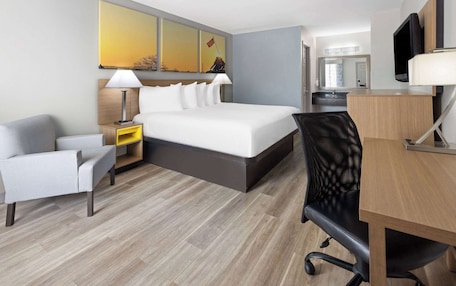 A hotel room with a bed, a desk, a chair, a nightstand, and a TV.