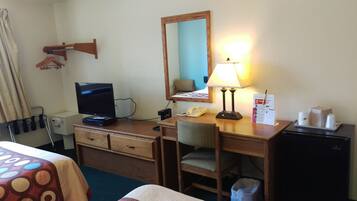 A hotel room with a desk, a television, a lamp, a telephone, and a small refrigerator.