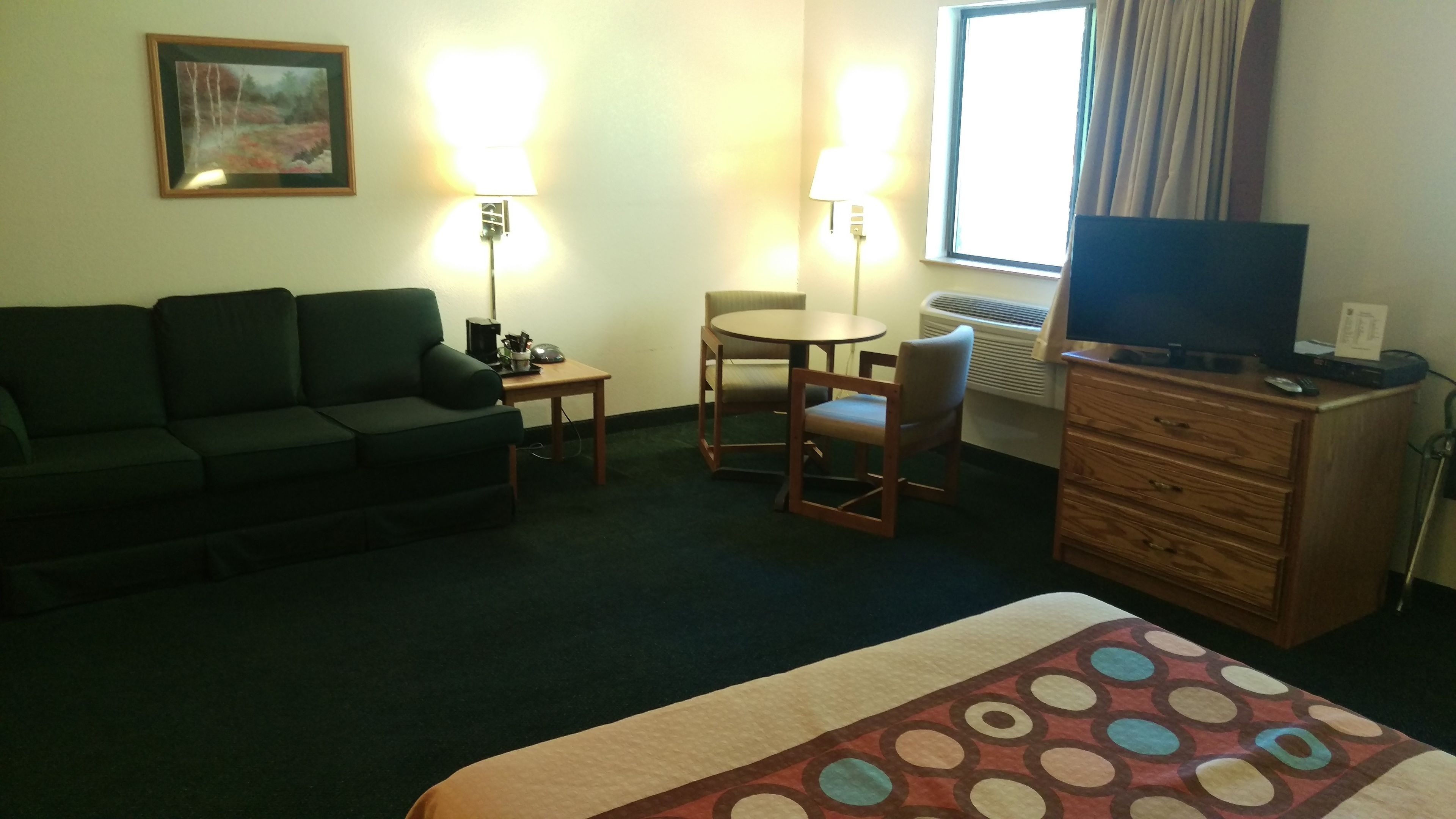 Una habitación de hotel con cama, sofá, una mesita, una silla, televisión y cómoda.