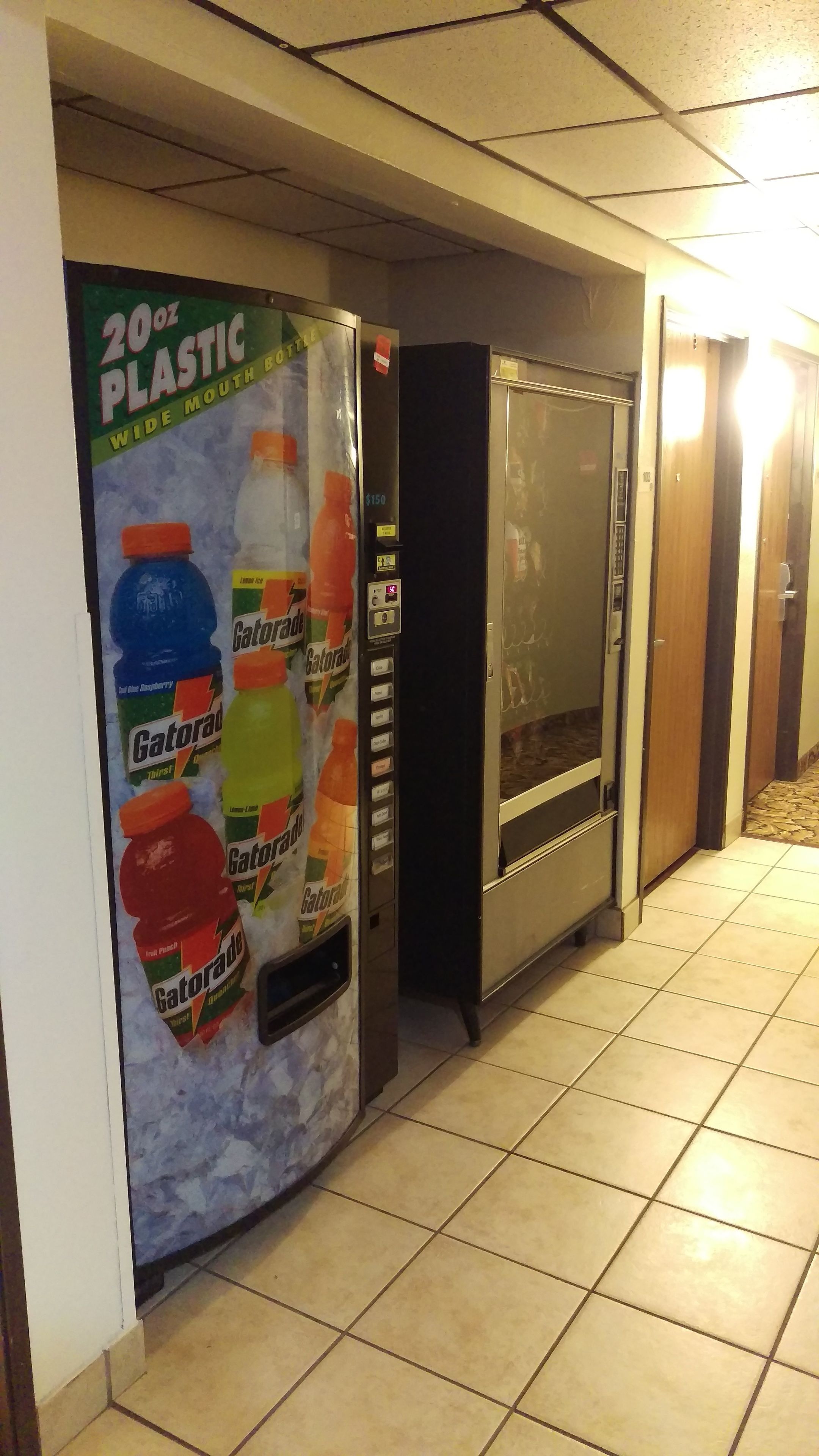 Una máquina expendedora con botellas de Gatorade y un refrigerador en un pasillo.