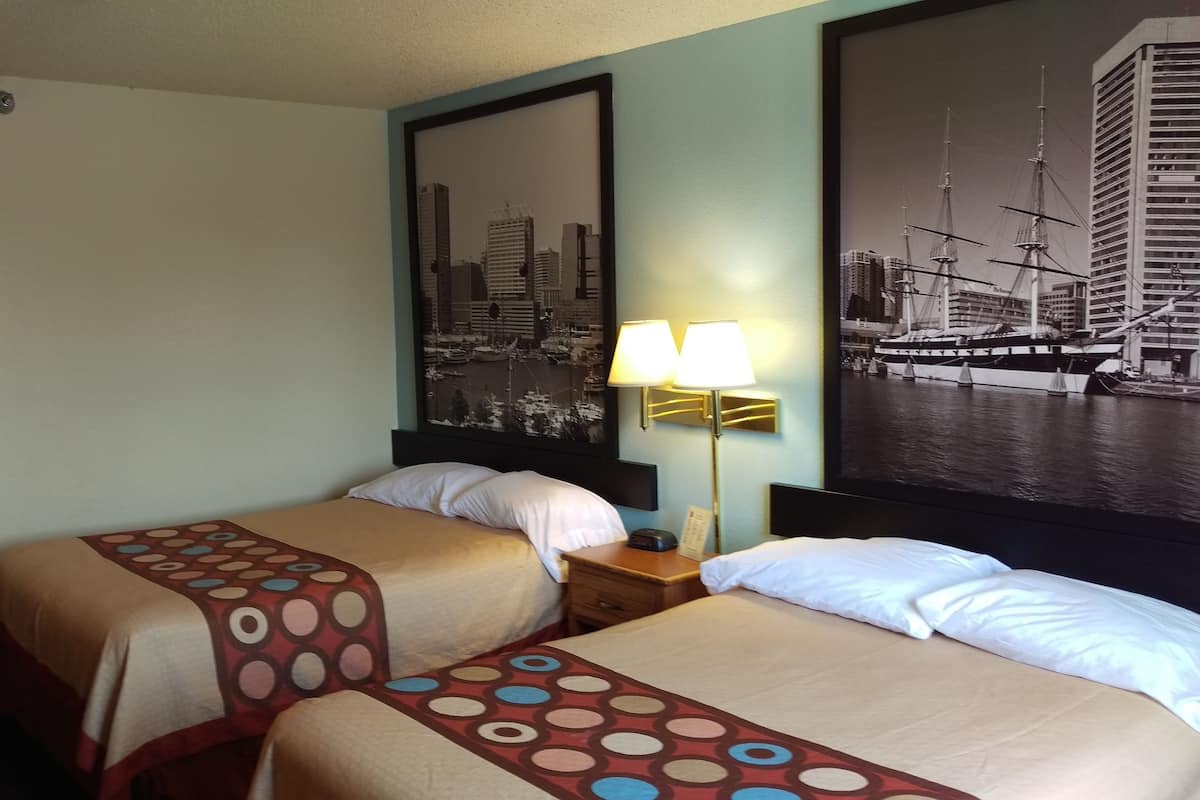 Quarto de hotel com duas camas, um espelho com vista para a cidade, uma luminária e um quadro com imagem de um navio.