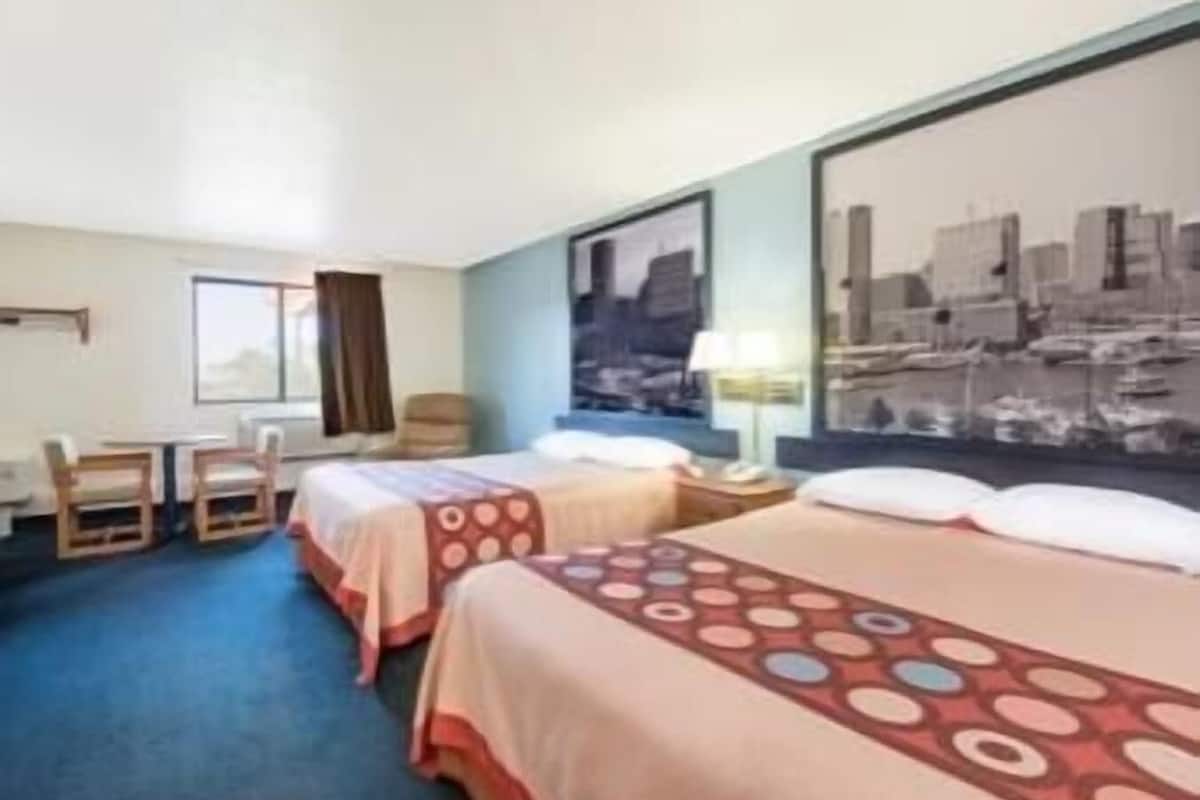 Quarto de hotel com duas camas, uma escrivaninha, uma cadeira, uma janela e uma pintura com vista para a cidade.