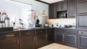 A kitchen with dark wooden cabinets, a trash bin labeled "TRASH", and a microwave.