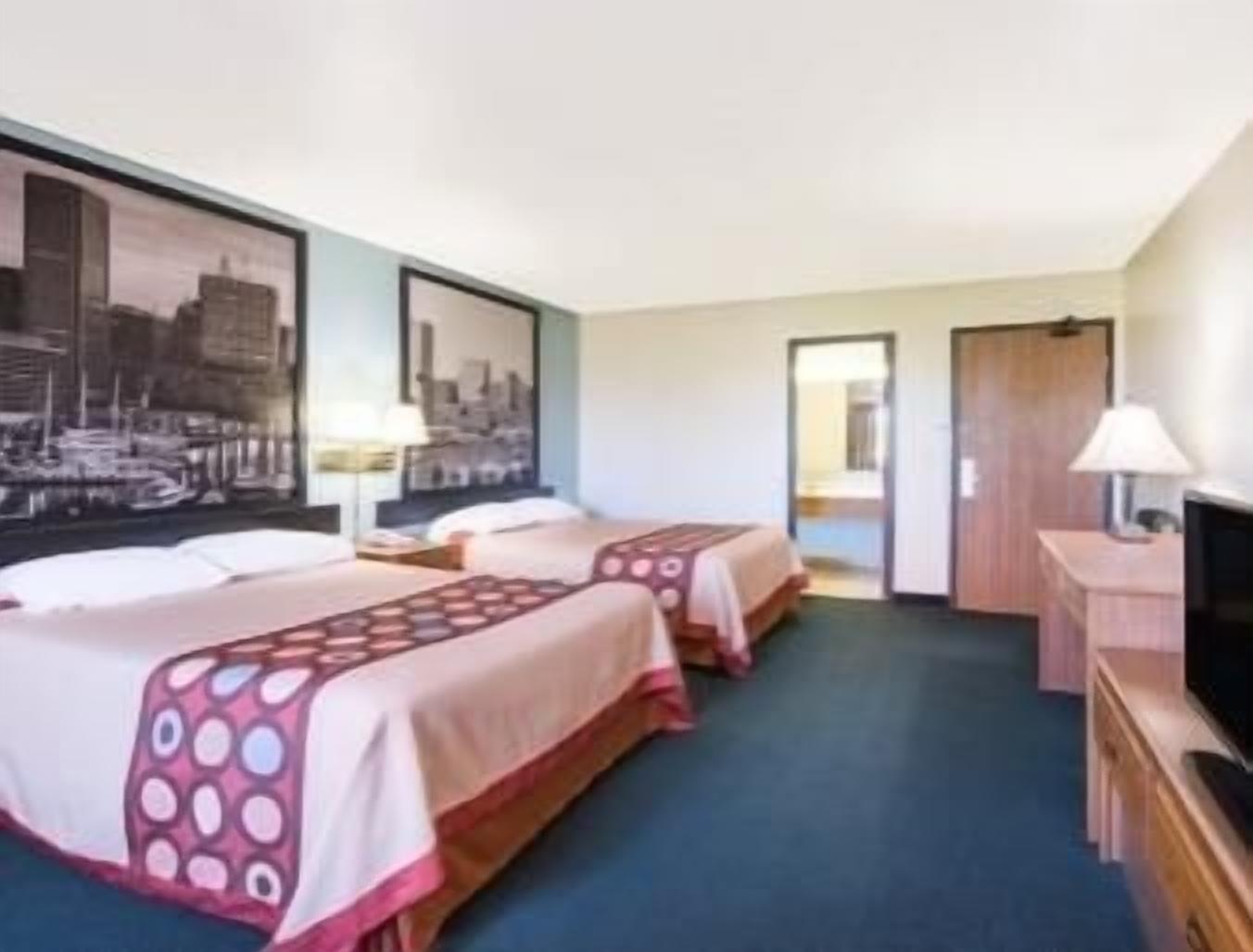 A hotel room with two beds, a television, a desk, and a large cityscape painting on the wall.