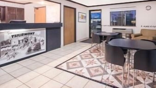 Un moderno vestíbulo de hotel con una mesa de recepción, piso de baldosas y un área de estar con mesas y sillas.