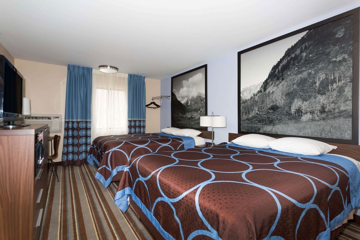 Une chambre d’hôtel avec deux lits, un bureau, une chaise, un porte-manteau et un grand tableau encadré au mur.