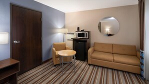 A hotel room with a wooden door, a sofa, a round mirror, a small table, a lamp, and a microwave.