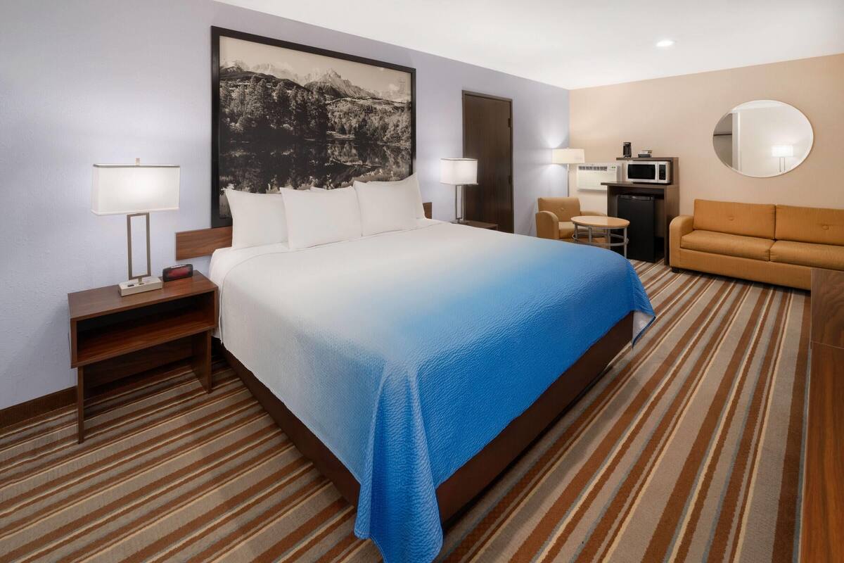 A hotel room with a large bed, a sofa, a desk with a computer, and a microwave.