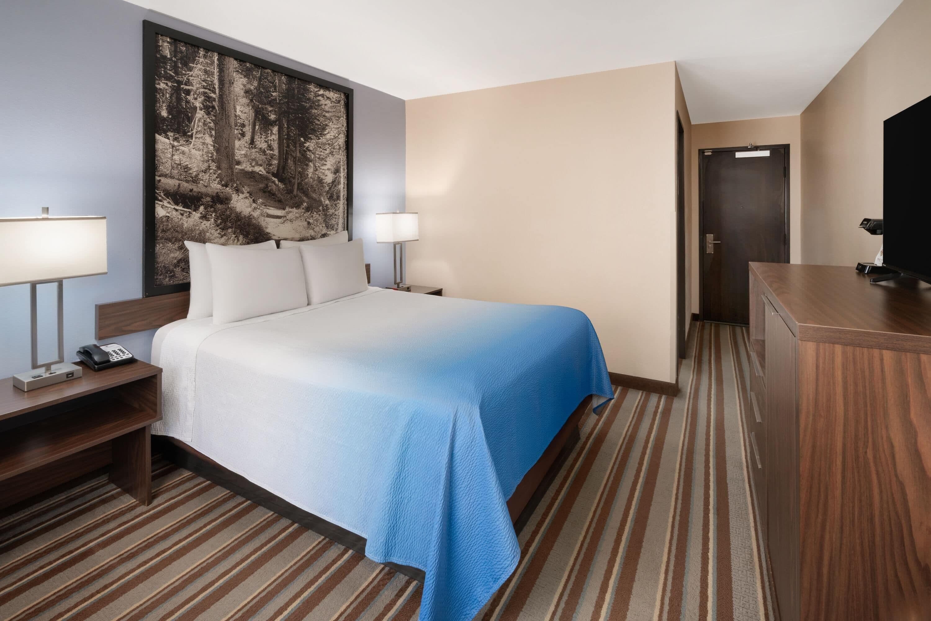 A hotel room with a bed, bedside lamps, a desk, a telephone, a television, and a door.