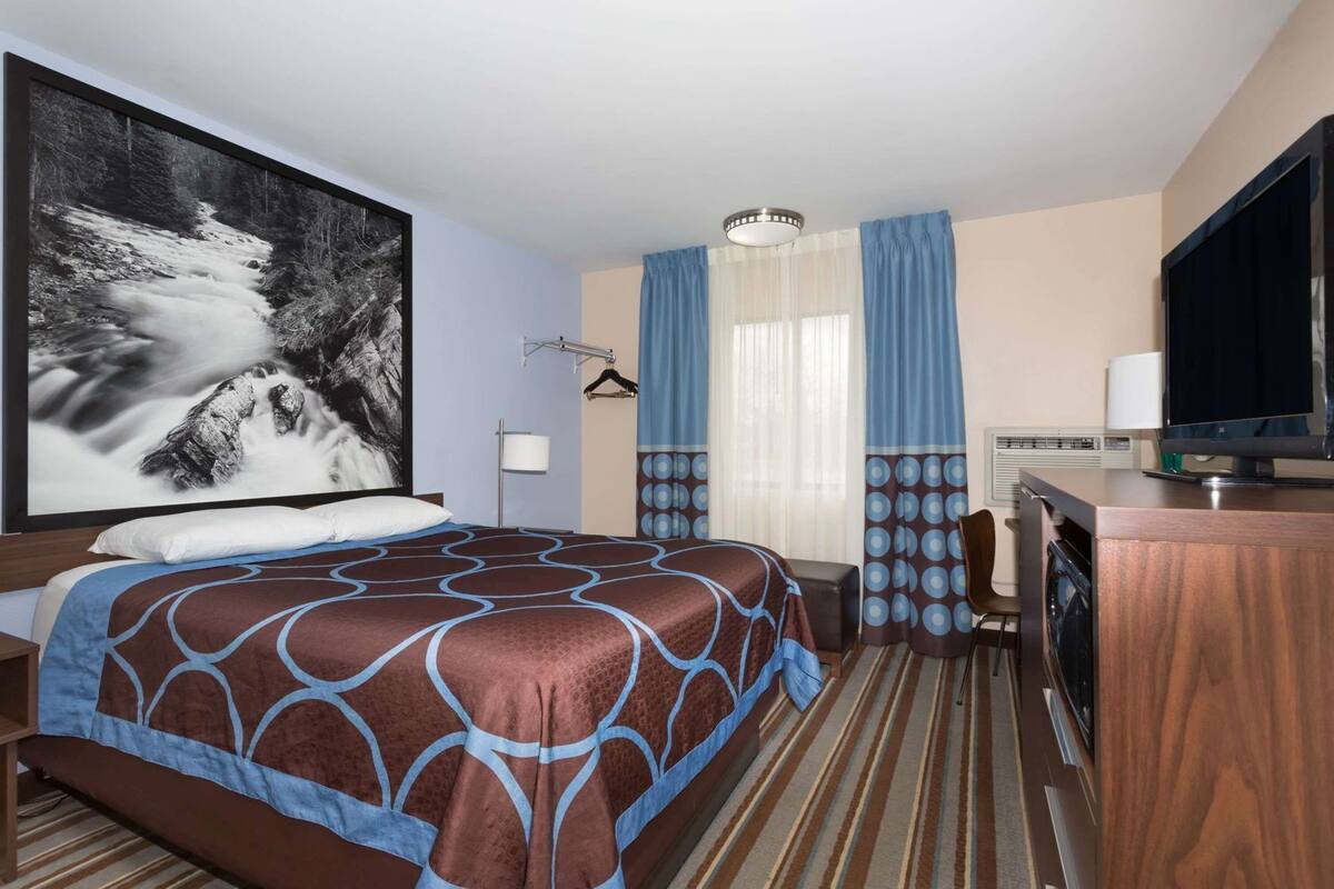A hotel room with a large bed, a desk, a television, and a painting of a waterfall.