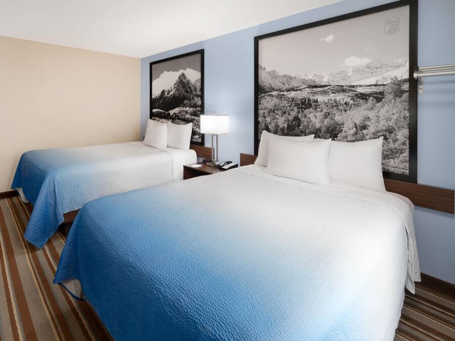 Ein Hotelzimmer mit zwei Betten, einem Streifenmuster-Teppich und zwei großen Landschaftsbildern an den Wänden.