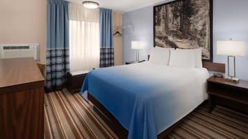 A hotel room with a bed, bedside tables, a desk, a chair, a hanging coat rack, a large painting, and a window with curtains.