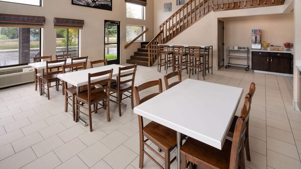 A spacious dining area with multiple tables and chairs, a staircase, and a kitchen area with a cart.