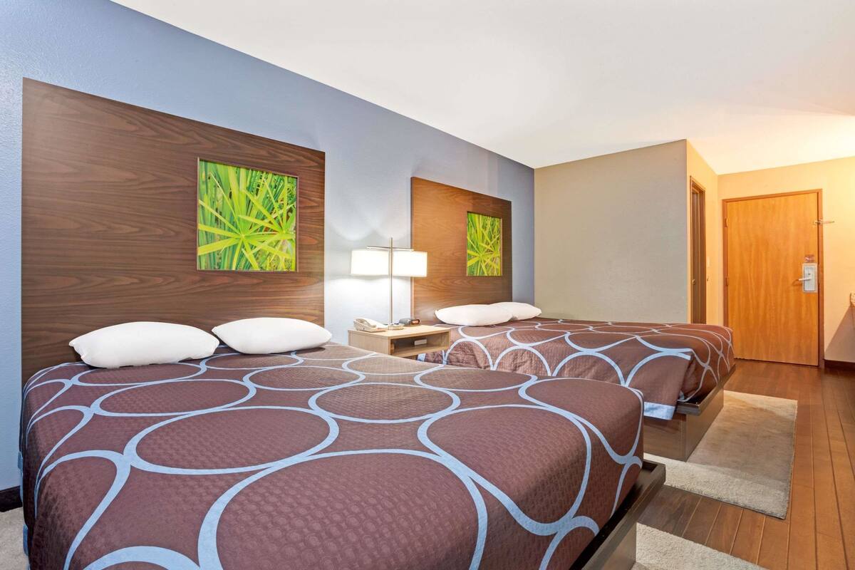 Una camera d'albergo con due letti, un comodino, una lampada e opere d'arte alle pareti.