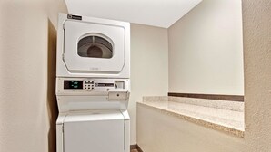 A compact, wall-mounted laundry machine with a digital display and control panel, situated in a corner of a room with a tiled floor and a small built-in bench. - Super 8 by Wyndham Louisville Airport (Louisville)