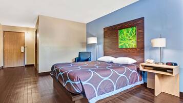 A hotel room with a bed, a desk with a lamp, a chair, and a painting on the wall.