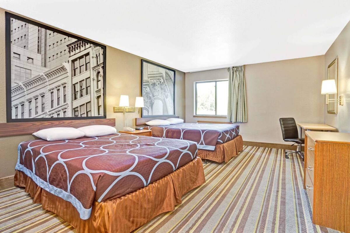 Camera d'albergo con due letti, una scrivania, una sedia, una lampada e un'ampia finestra.