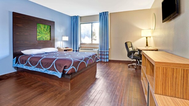 A hotel room with a bed, a desk, a chair, a TV, and a window with curtains. - Super 8 by Wyndham Louisville Airport (Louisville)